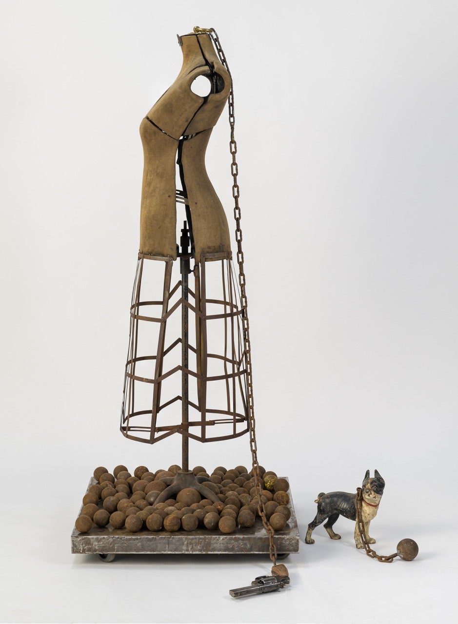 sculpture of woman and dog, both chained to metal balls